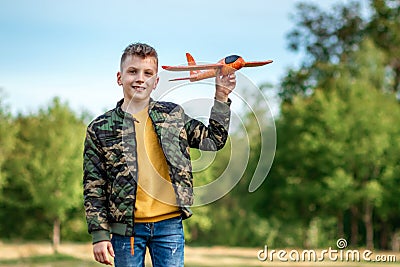 The boy launches a toy airplane against the backdrop of greenery. The concept of dreams, choice of profession, pilot, childhood. Stock Photo