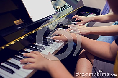 A boy is learning piano with woman teacher and music notation on tablet, four hands from two people playing piano Stock Photo