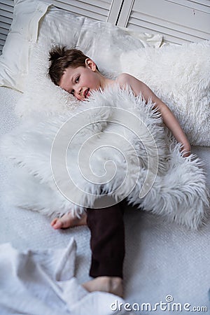 Boy lies on bed with white bedding, handsome young man with pretty face is resting in bed, cozy sleeping place Stock Photo