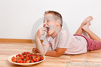 Boy lies on the floor and eats ripe strawberry berries Stock Photo