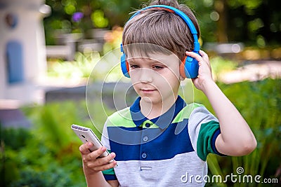 Boy listening music in headphones sitting on the bench and stares at the phone. Warm sunny evening. music relax concept Stock Photo