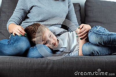 The boy is lying on the couch with an abdominal pain near his mother. The concept of custody, parental care, stomach problems, Stock Photo