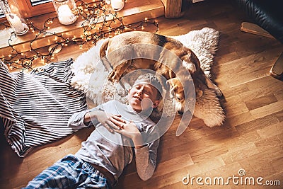 Boy lying on the floor and near beagle dog sleeping on sheepskin in cozy home atmosphere Stock Photo