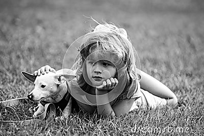 Boy lying on grass with dog. Happy puppy owner child playing with doggy on lawn. Stock Photo