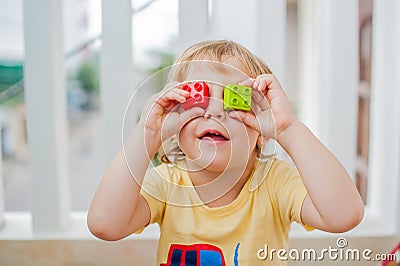 The boy makes eyes of colorful children`s blocks. Cute little kid boy with glasses playing with lots of colorful plastic Stock Photo