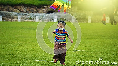 Boy with mask flying a kite at a park. Boy holding a colorful kite standing over green grass.SETIA ALAM,SELANGHORE,MALAYSIA:09/20/ Editorial Stock Photo