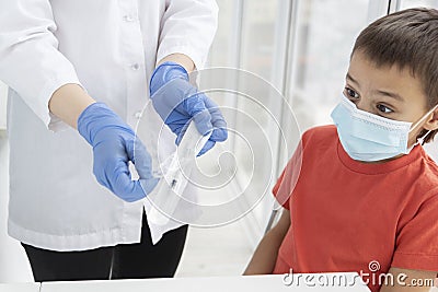 Boy in medical mask is afraid of coming vaccination looking with surprise at doctor`s hands opening syringe pack. Stock Photo