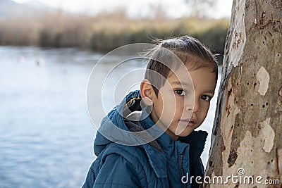 A boy near the tree by the river with expressionless gaze Stock Photo