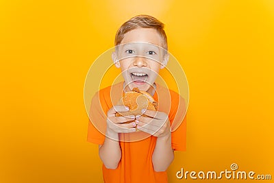 Boy in an orange T-shirt holds a hamburger in front of him and laughs loudly against a yellow background Stock Photo