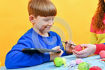 A boy paints Easter eggs with a paintbrush with the help of his older sister Stock Photo