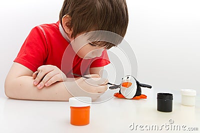 Boy paints a penguin made of salty dough Stock Photo