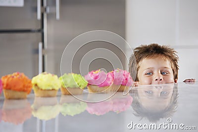 Boy Peaking Over Counter At Row Of Cupcakes Stock Photo
