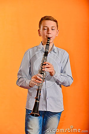 The boy performs solo at a concert, plays the clarinet on an orange background Stock Photo