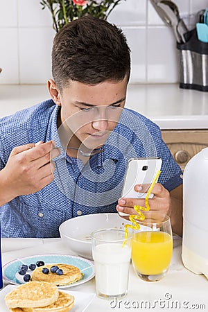 Boy with phone having breakfast in kitchen Stock Photo