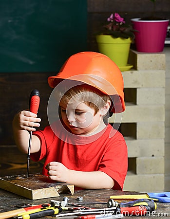 Boy play as builder or repairer, work with tools. Kid boy in orange hard hat or helmet, study room background. Childhood Stock Photo