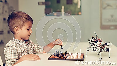 Boy Playing Chess with a Small Robot at Table. Stock Photo