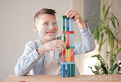 Boy is playing with colored wooden bricks by building tower. Motor skills improvement Stock Photo