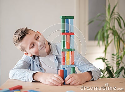 Boy is playing with colored wooden bricks by building tower. Motor skills improvement Stock Photo