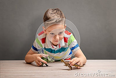 Boy is playing with dinosaurs on desk. Concept of dinosaur obsession Stock Photo