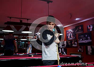 Boy plays billiard or pool in club. Young Kid learns to play snooker. Boy with billiard cue strikes the ball on table. Stock Photo