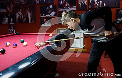 Boy plays billiard or pool in club. Young Kid learns to play snooker. Boy with billiard cue strikes the ball on table. Stock Photo