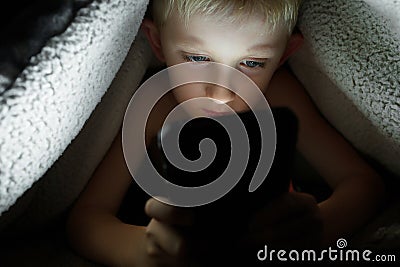 Boy plays games on a smartphone at night under a blanket on the floor Stock Photo