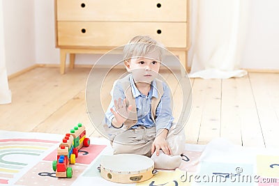 The boy plays with a musical wooden drum and a train. Educational wooden toys for the child. Portrait of a boy sitting on the floo Stock Photo