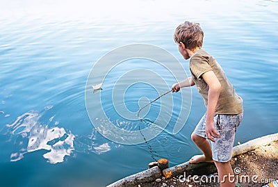 Boy plays with paper boat and launches it on the lake Stock Photo