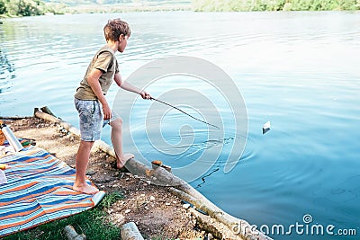 Boy plays with paper boat and launches it on the lake Stock Photo