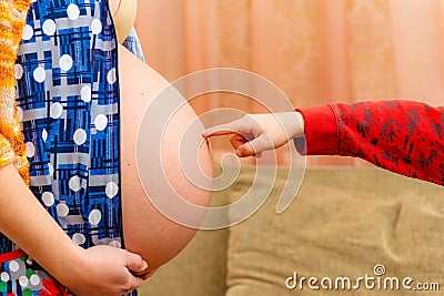 The boy pokes a finger in the big belly of a pregnant mother Stock Photo