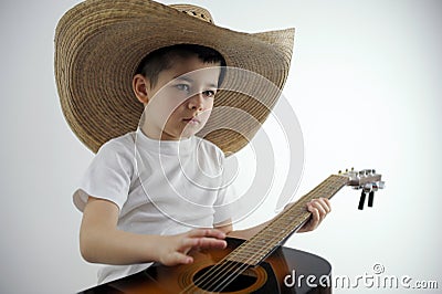 boy of preschool age in hands with guitar in large Mexican hat sits on white background looks thoughtfully invents Stock Photo