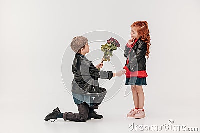 boy presenting roses bouquet to his little girlfriend while standing on knee Stock Photo