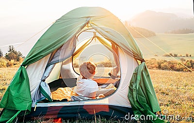 Boy rest in camping tent and enjoy with sunset light in mountain valley Stock Photo