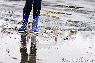 Boy in rubber blue rainboots jumping to dirty puddle Stock Photo