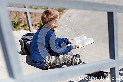 Boy schoolboy sits on the steps and reads a book Stock Photo