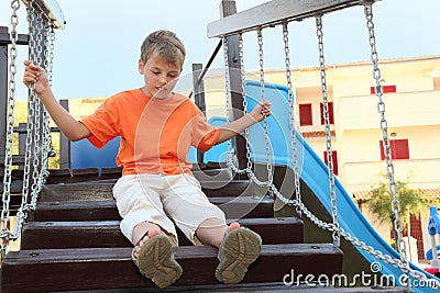 Boy in shirt sitting on suspension bridge Stock Photo