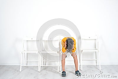 The boy sits on a chair with his head down, and holding it with Stock Photo