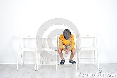 The boy sits on a chair with his head down. He is somewhat upse Stock Photo