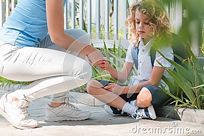 Boy sits cross-legged on the curb, an anonymous woman crouches beside him Stock Photo