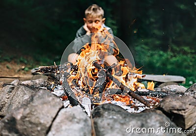 Boy sits near campfire in forest Stock Photo