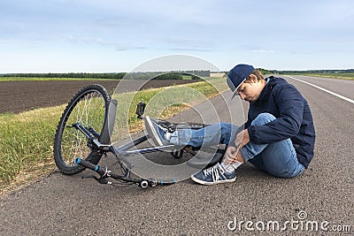 Boy sits in a road after falling from a bike, calms the pain in her knee Stock Photo