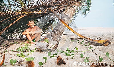 Boy sits in selfmade hut on the tropical beach and plays in Robinzone Stock Photo