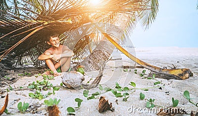 Boy sits in selfmade hut on the tropical beach and plays in Robinzone Stock Photo