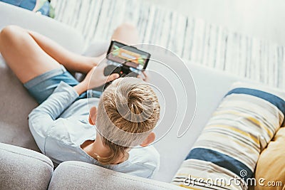 Boy sits on sofa plays with smartphone and gamepad camera top view. Child and electronic devices concept Stock Photo