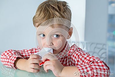 Boy sits at the table and eats a chocolate bar Stock Photo