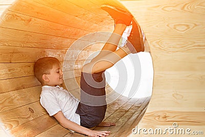 Boy sits in a wooden tunnel with legs up. Eco-friendly natural playground. Soft light Stock Photo