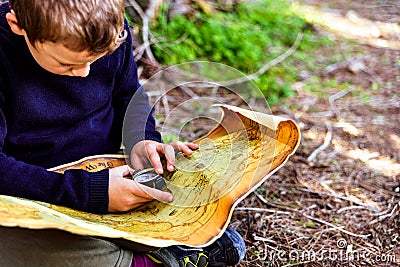 Boy sitting on the forest floor using a compass on an old map Stock Photo