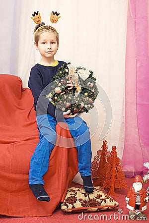 Boy sitting on red chair with Christmas wreath in his hands Stock Photo