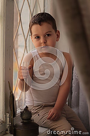 The boy is sitting on the window sill. Sad mood. Sit at home. Stock Photo