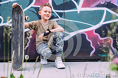 Boy with skateboard sits near graffiti painted wall Stock Photo